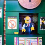 A Lego sculpture of an MTA employee in an old-fashioned token booth clerk, with the old NYC subway toekn above. There's also a sign that says the J is not working and a subway map of midtown.